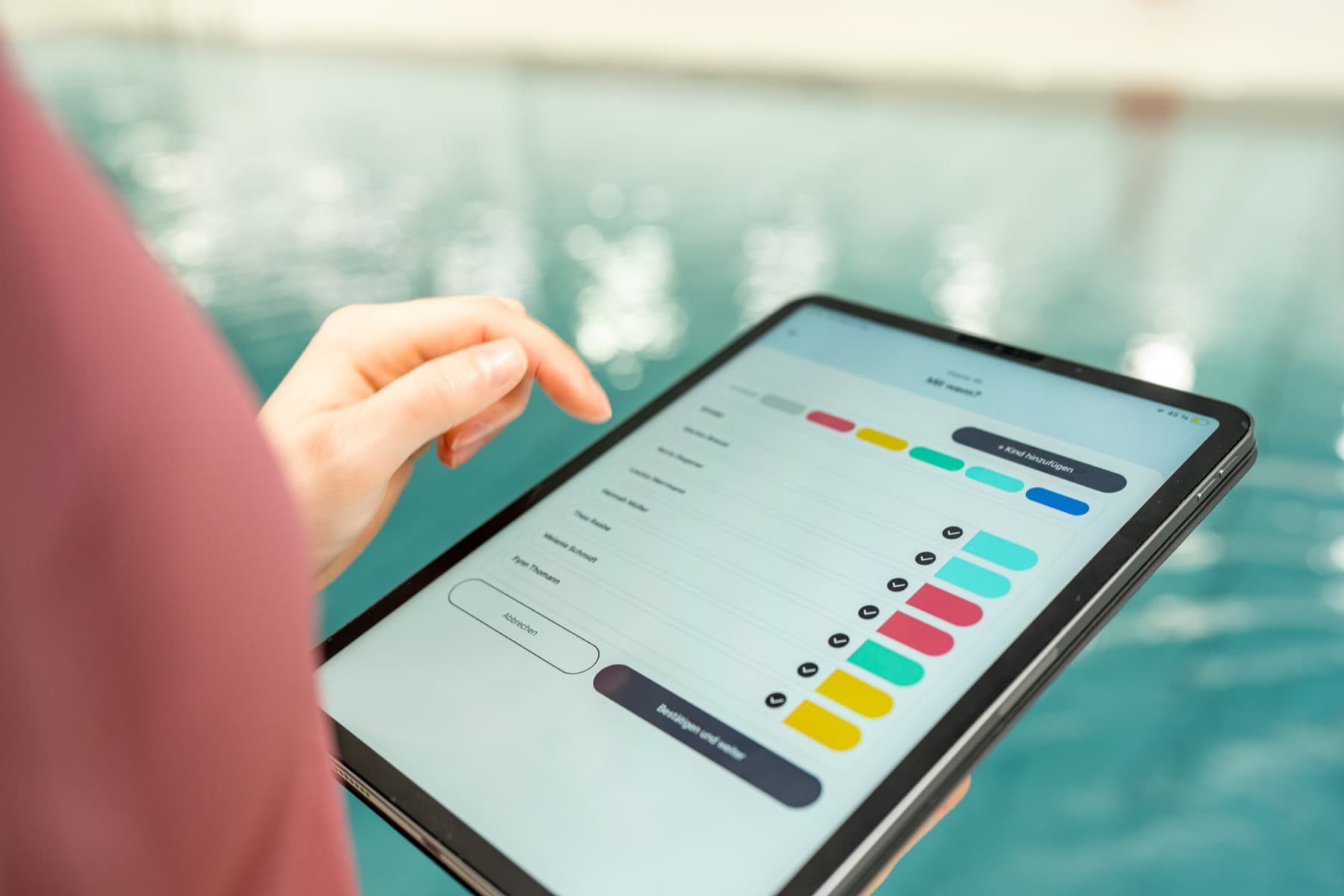 Tablet mit der Schwimm-Lehr-App Schuhuu am Beckenrand, darauf eine Liste mit farbigen Bewertungsbalken